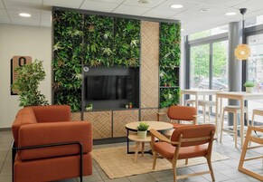 Un intérieur moderne avec des sièges orange, une table ronde, un écran de télévision et un mur vert agrémenté de plantes.
