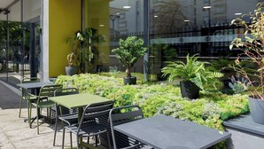 An outdoor seating area with tables and chairs, surrounded by potted plants and greenery.