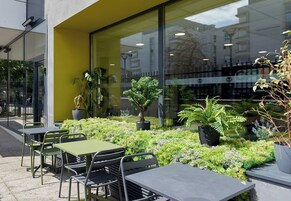 Un espace extérieur aménagé avec des tables et des chaises, entouré de plantes en pot et de verdure.