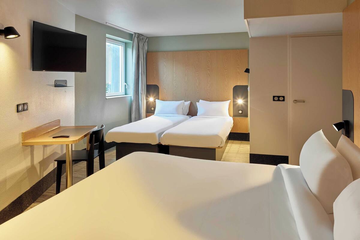 A hotel room with a large bed, a desk, a TV, and a window with curtains.