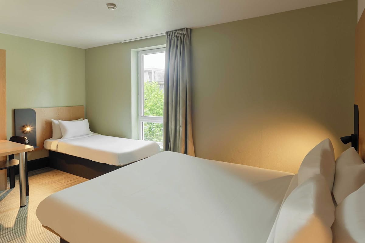 A hotel room with two beds, a desk, and a window with curtains.