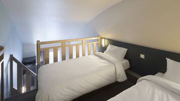 A hotel room with two single beds, a wooden headboard, a dark wall, and a staircase leading to an upper level.