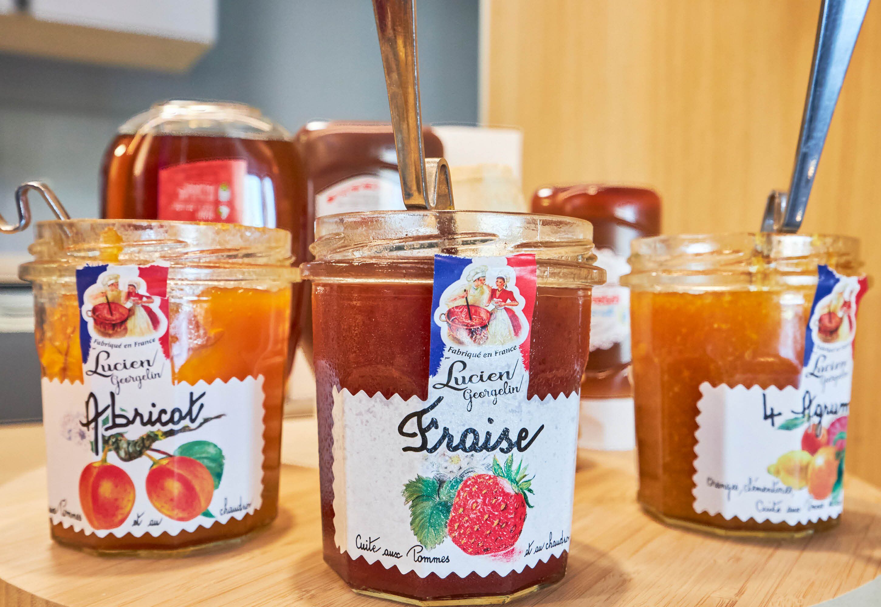 Drei Gläser mit Früchtekonserven von Lucien Georgeselin auf einer Holzoberfläche.