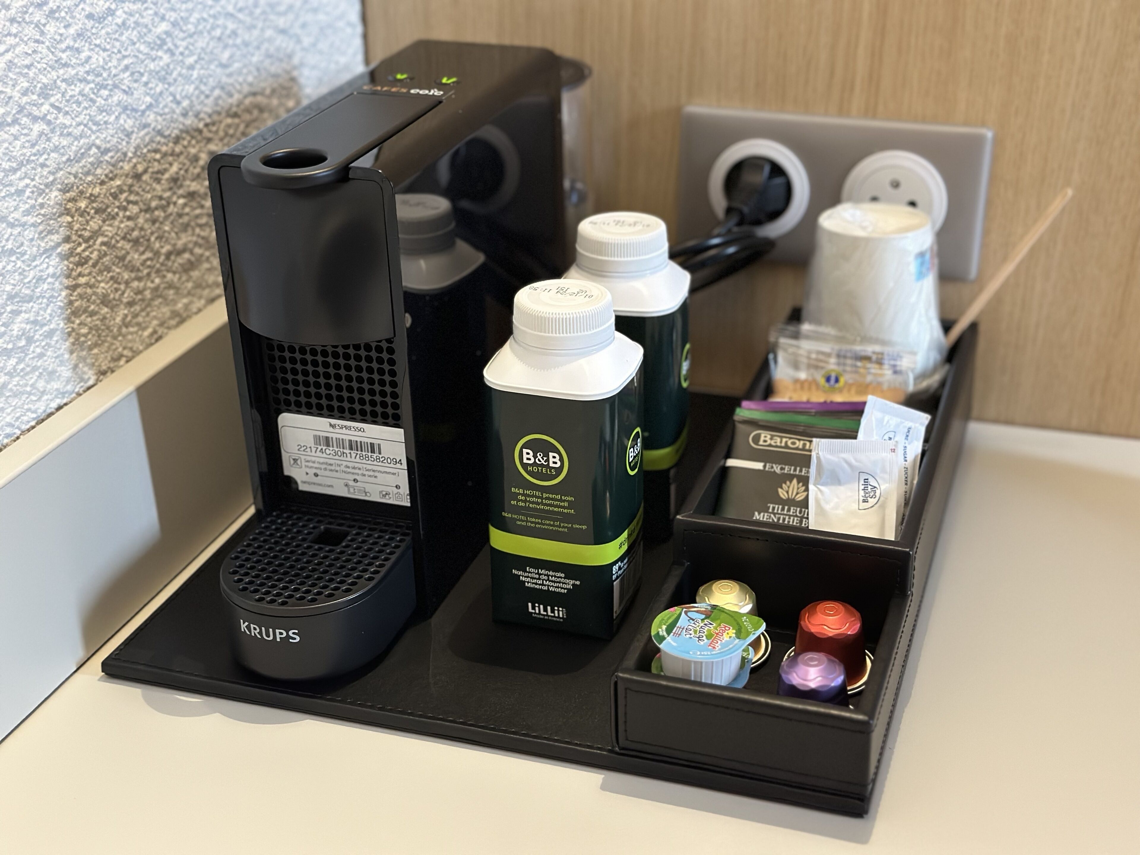 A coffee station with a Krups coffee maker, B&B Hotels branded bottles, and a variety of tea and coffee pods.