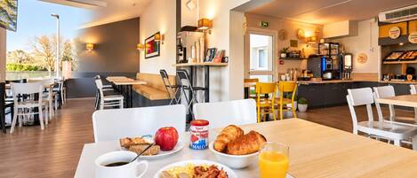 A breakfast setting with a table, chairs, and a variety of food items including croissants, eggs, bacon, and a glass of orange juice.