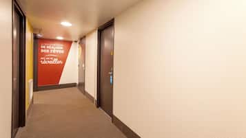 A hotel hallway with carpeted floors, a red wall with French text, and doors with a blue sign.