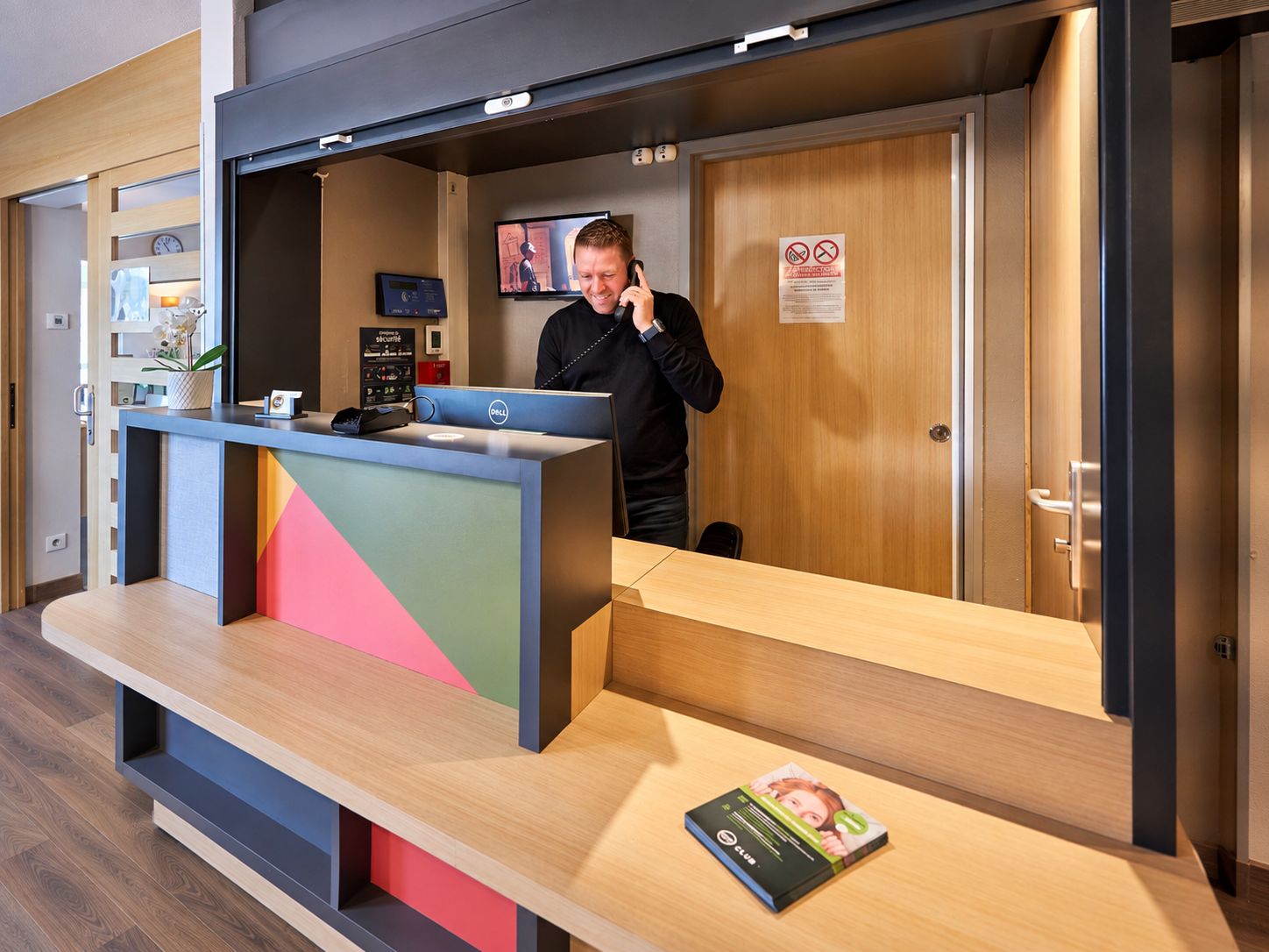 Ein Hotelrezeptionstresen mit modernem Design, einem digitalen Display und einem Schild, das Rauchen untersagt.