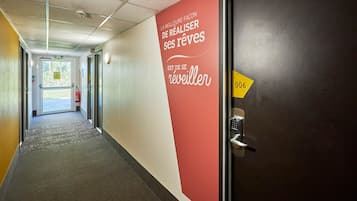 Un couloir d’hôtel avec un mur rouge orné d’un texte motivant, une porte portant un numéro et un extincteur fixé au mur.