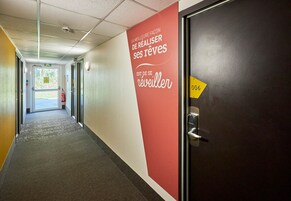 Pasillo de hotel con una pared roja que muestra texto motivacional, una puerta con un letrero de número y un extintor en la pared.