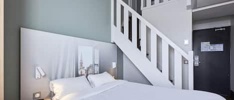 Une chambre d’hôtel comprenant un lit, une table de chevet, un miroir fixé au mur, un escalier et une porte avec une serrure.