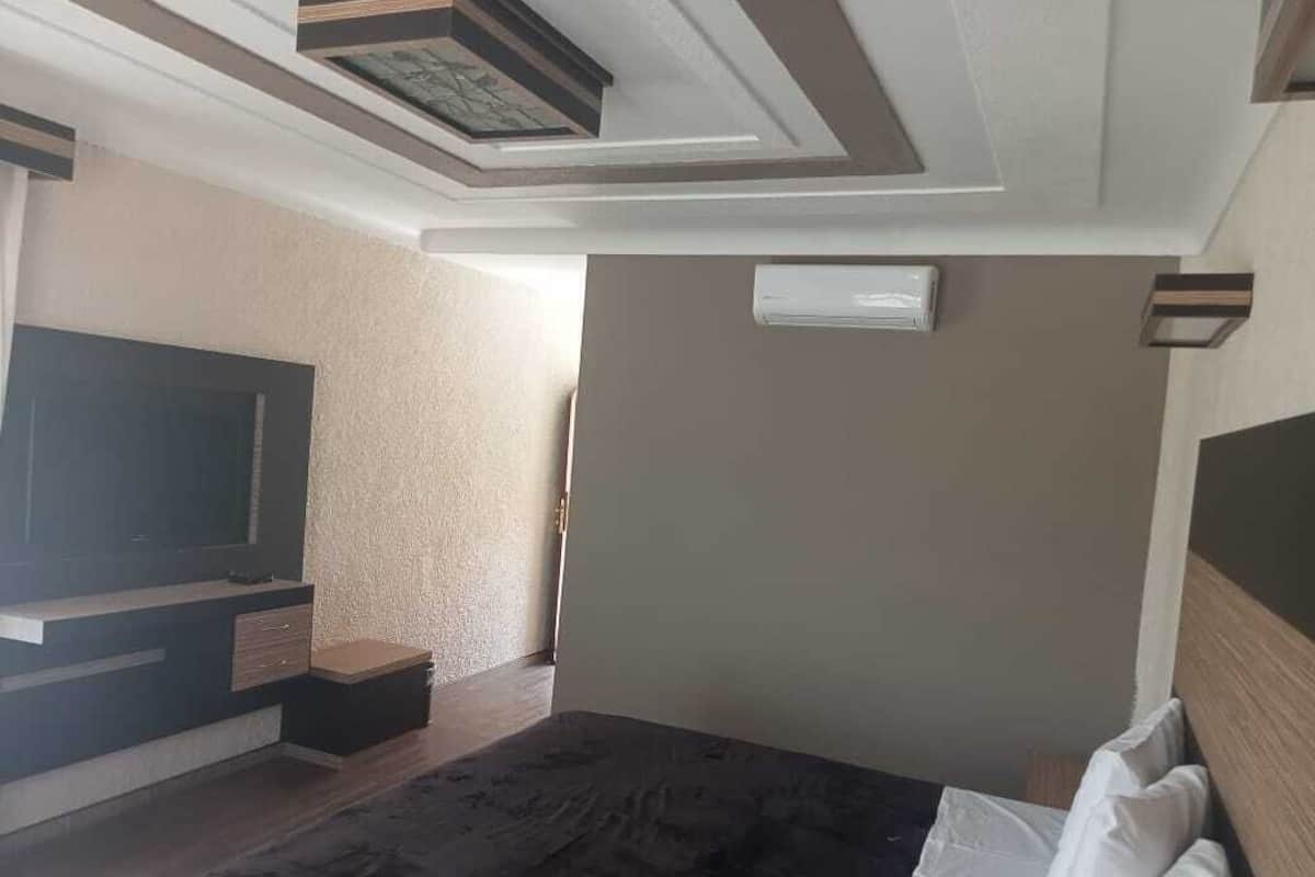 A bedroom with a bed, a TV, a wall-mounted air conditioner, and a ceiling with a geometric design.