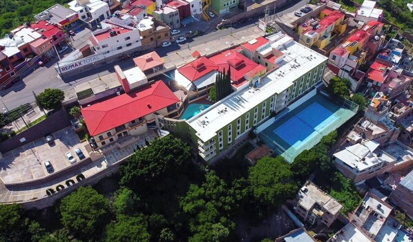An aerial view of a building with a swimming pool, surrounded by other buildings and greenery.