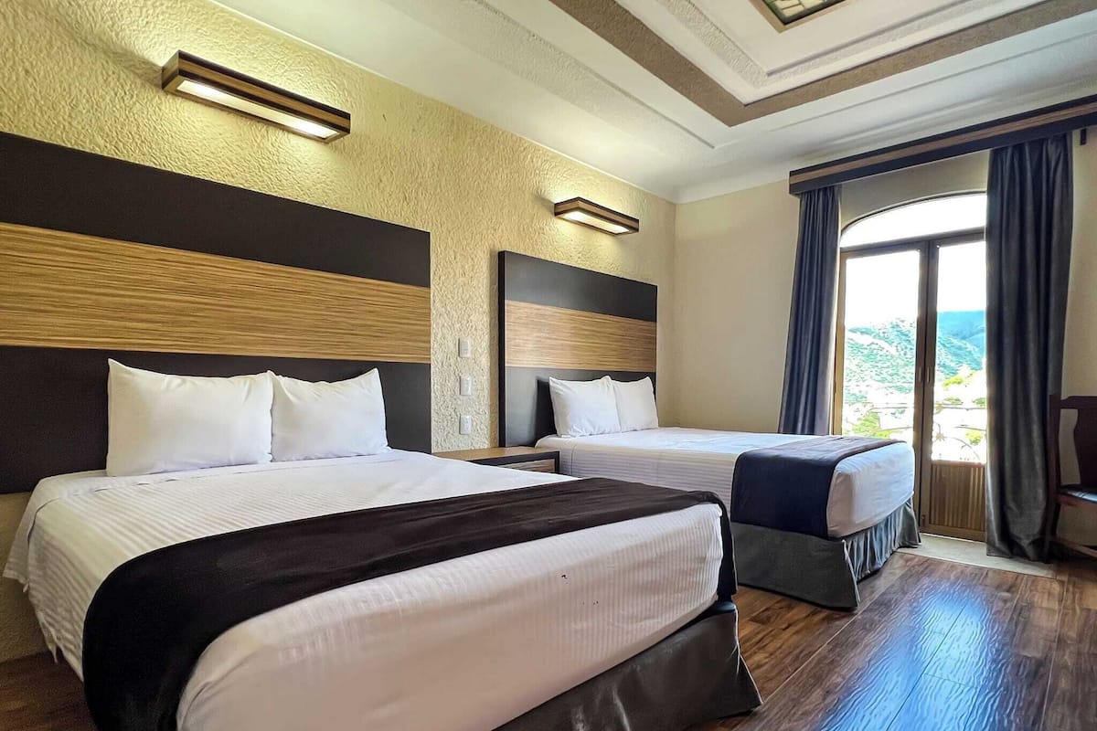 A hotel room with two beds, wooden flooring, and a large window with a view.
