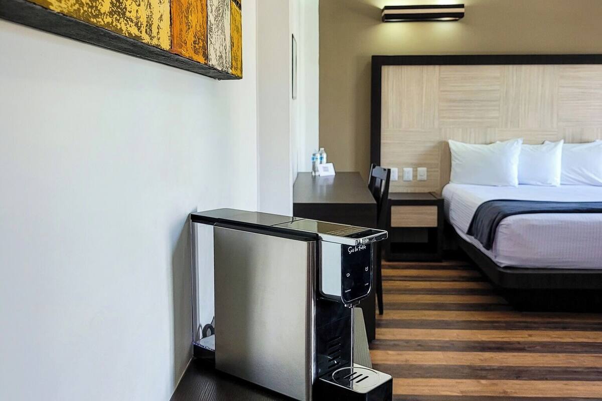 A hotel room with a bed, bedside table, coffee maker, and a painting on the wall.
