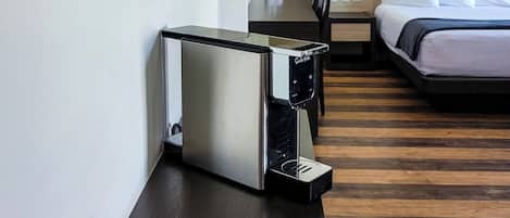 A hotel room with a bed, bedside table, coffee maker, and a painting on the wall.