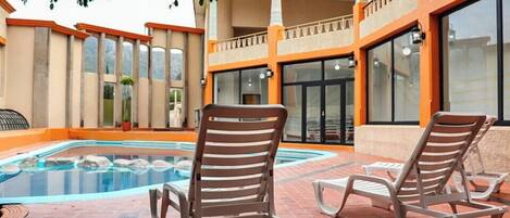 A swimming pool area with lounge chairs and a tiled deck.