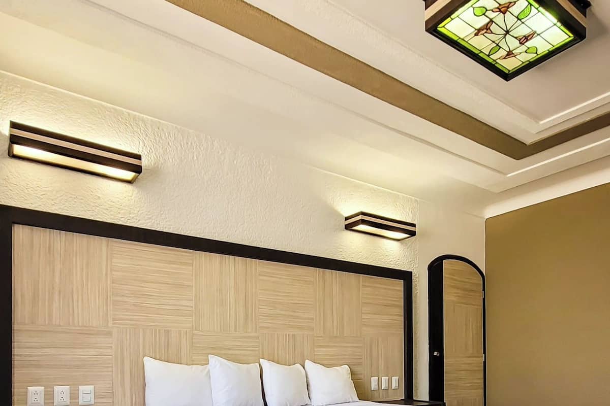 A neatly made bed with a dark headboard and white bedding, a bedside table with a drawer, and a wall-mounted light fixture above the bed.