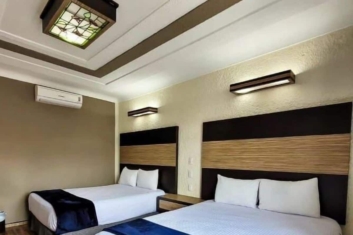 A hotel room with two beds, a ceiling light fixture, an air conditioning unit, and a wall-mounted light.