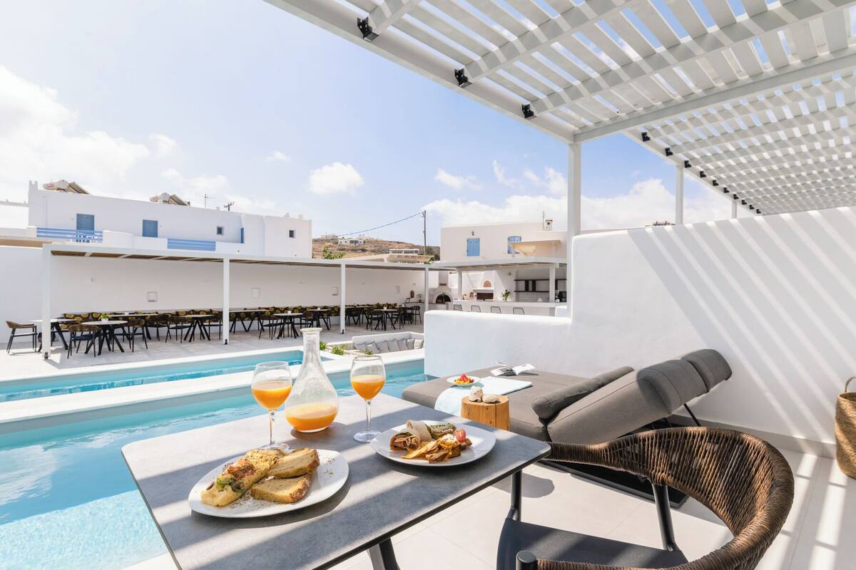 A rooftop pool area with dining tables, lounge chairs, and a view of the surrounding buildings.