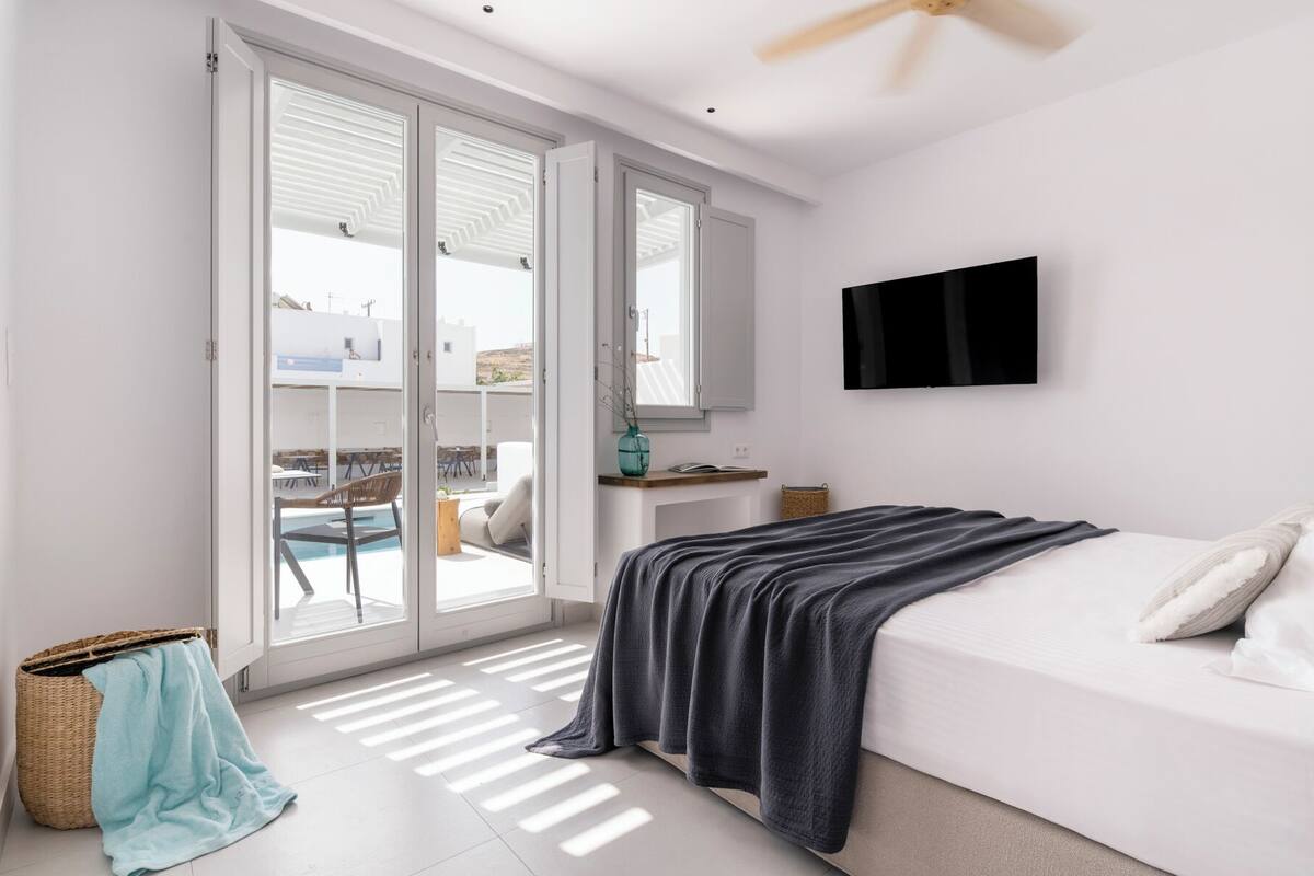 A modern bedroom with a bed, a TV, and a balcony with outdoor furniture.