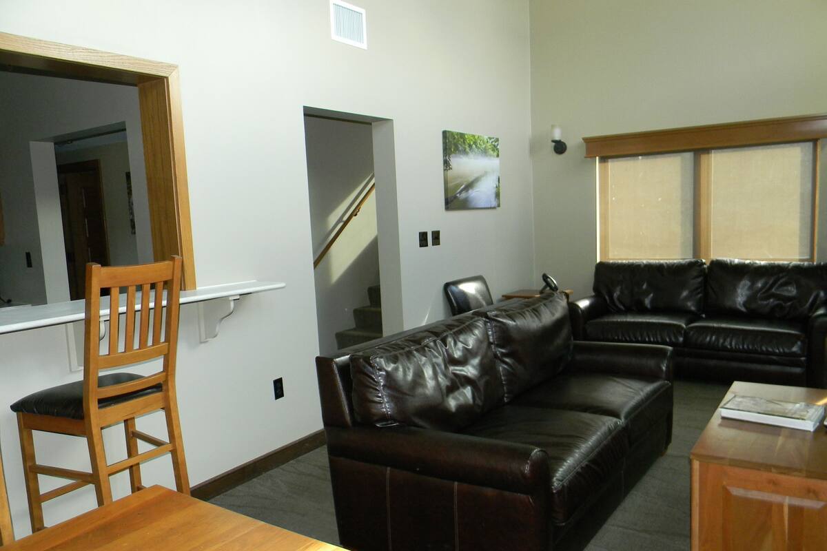 A living room with a wooden dining table, a leather sofa, and a wooden chair.