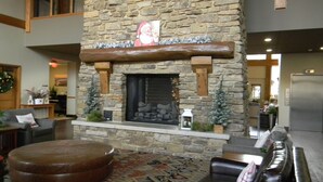 Una chimenea de piedra con un cuadro navideño encima, un reposapiés de cuero y una alfombra estampada.