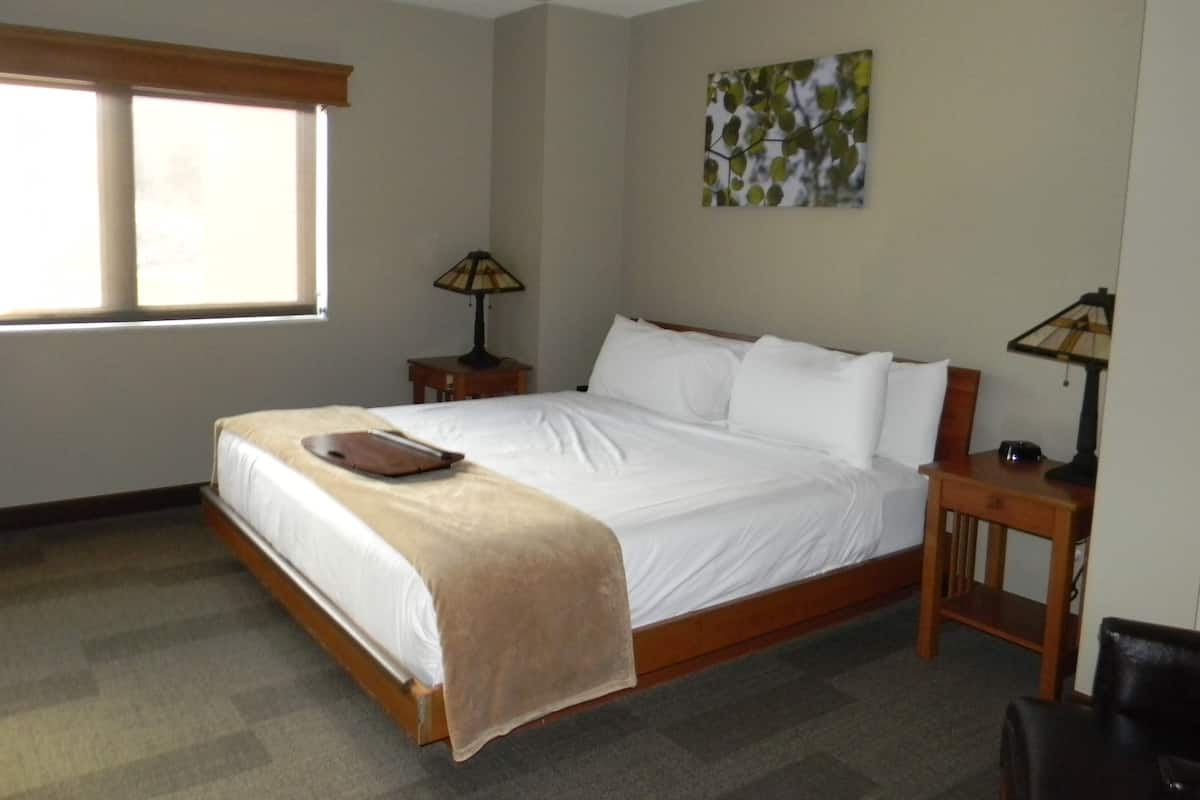 A hotel room with a large bed, two bedside tables with lamps, a window, and a painting on the wall.