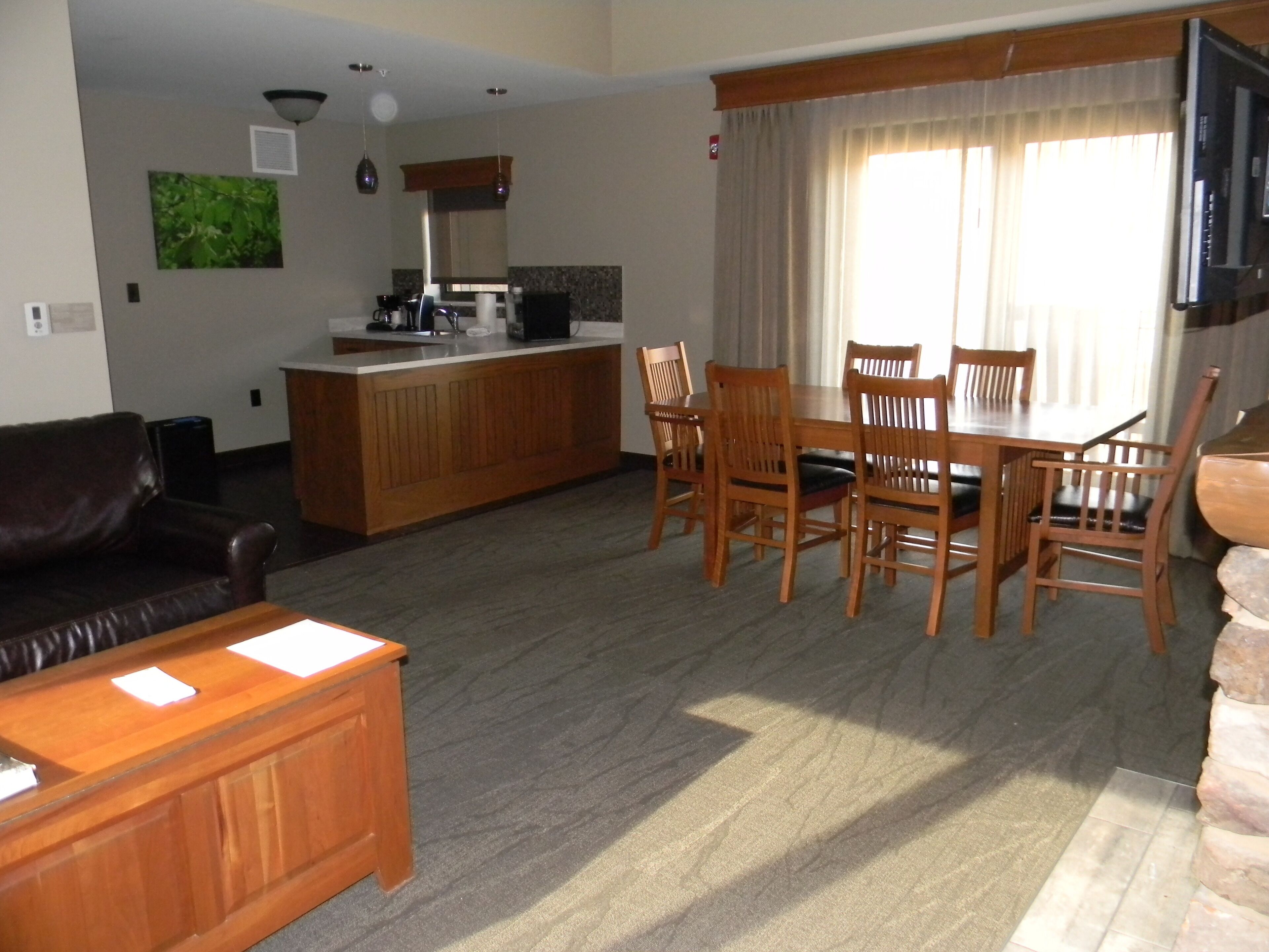 A living room with a wooden coffee table, a brown leather sofa, and a dining area with wooden chairs and a table.