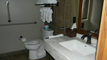 A bathroom with a white toilet, a sink with a mirror, a towel rack with folded towels, and a handrail.
