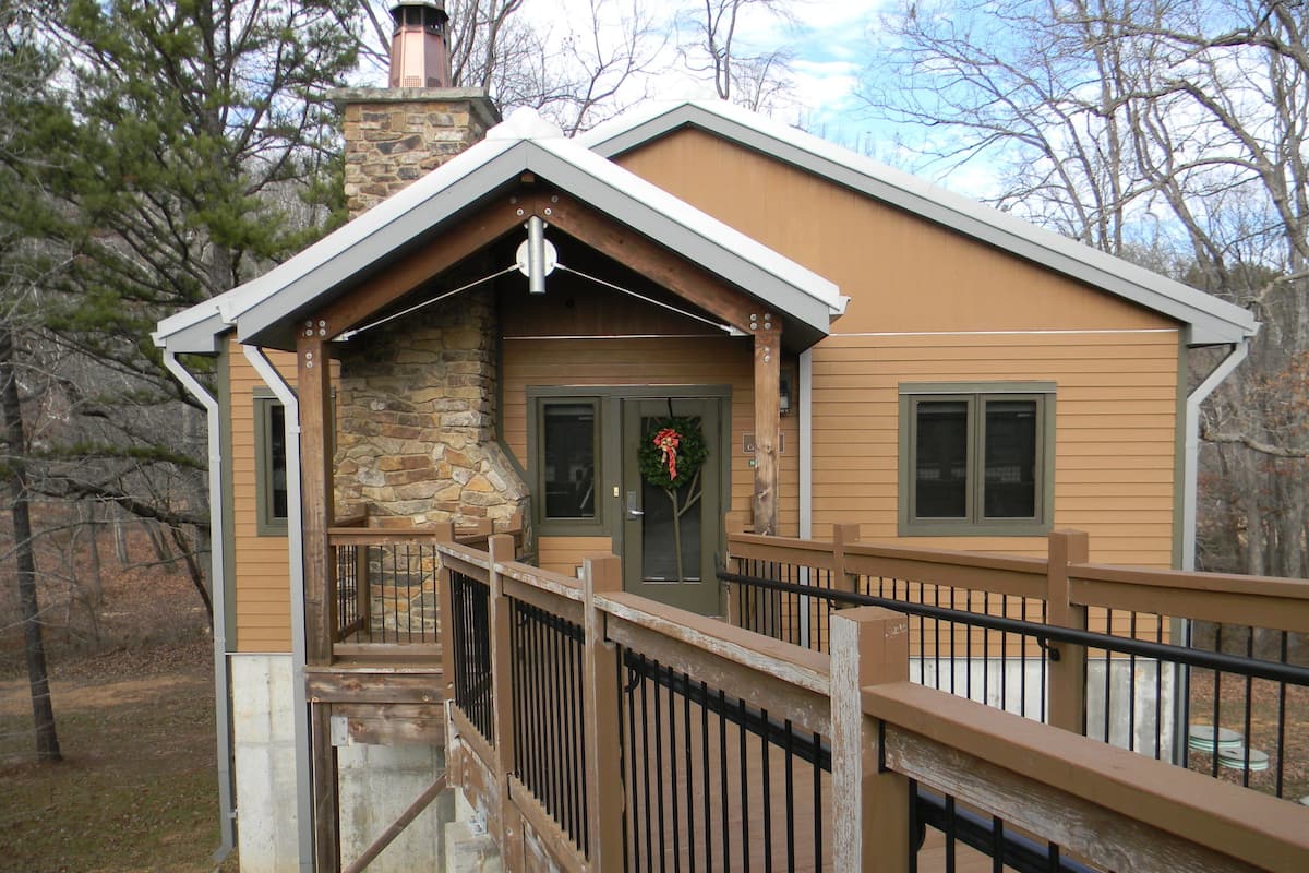A lodge with a stone chimney, a wooden deck, and a door with a wreath.