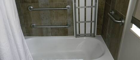 A bathroom with a bathtub, grab bars, and a shower curtain.
