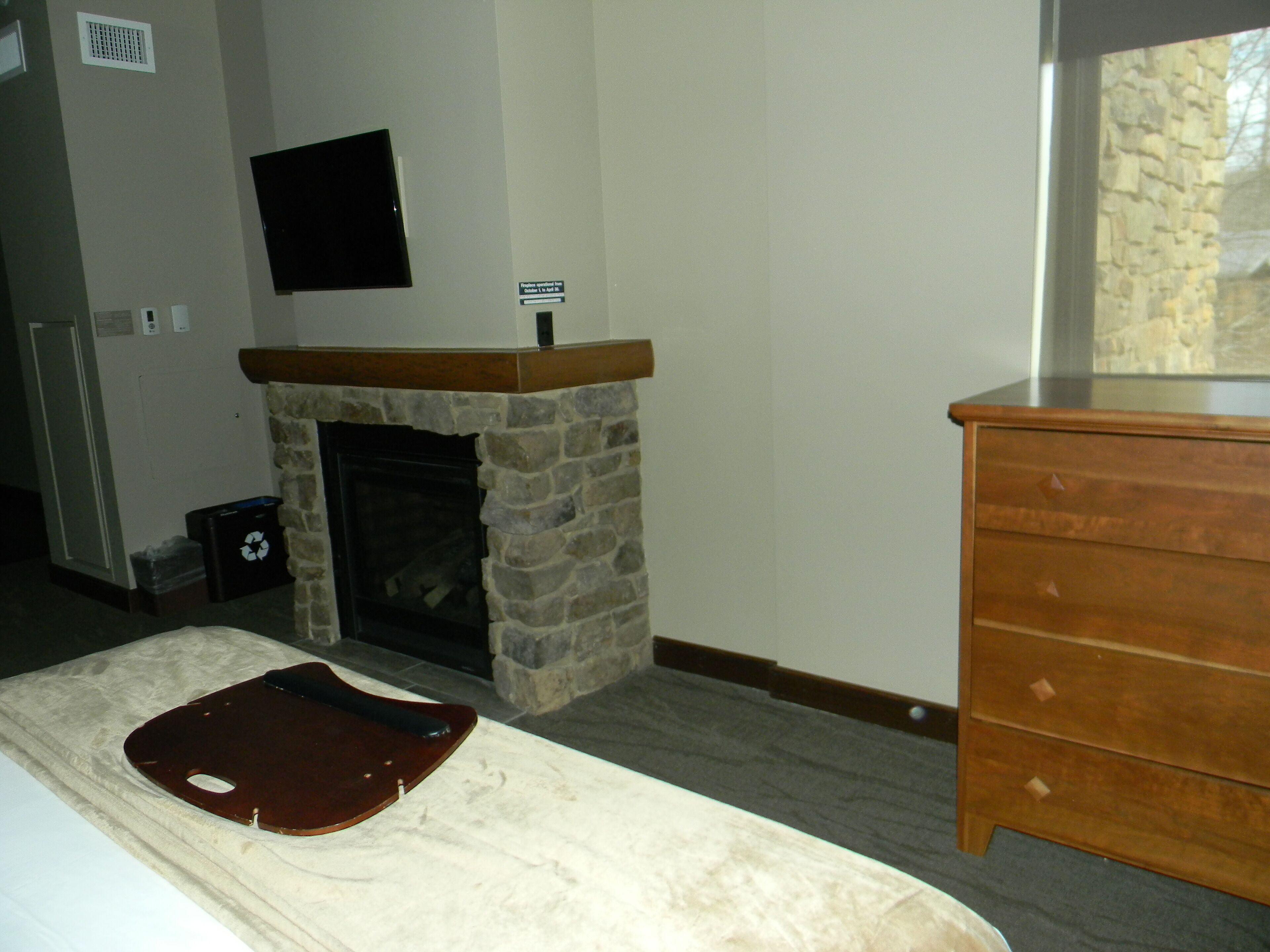 A room with a stone fireplace, a wooden dresser, and a bed with a brown headboard.