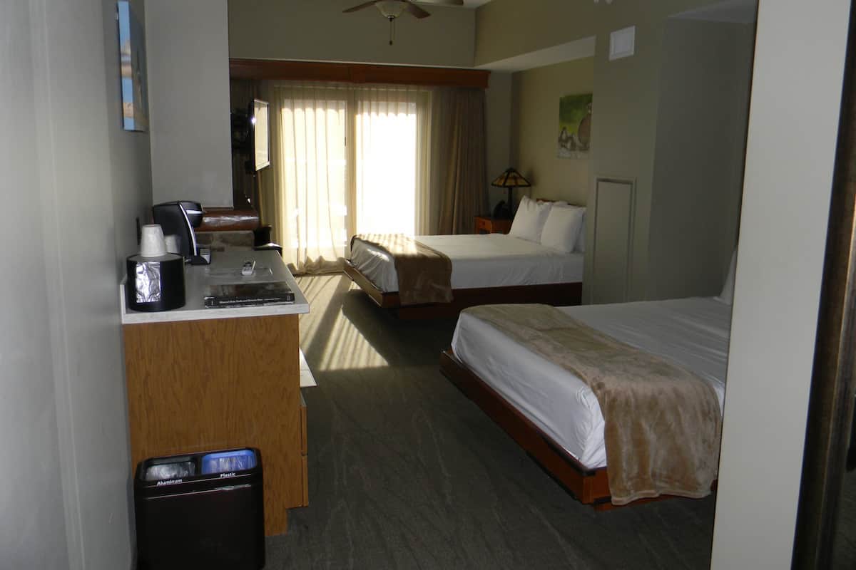 A hotel room with two beds, a desk with a coffee maker, and a ceiling fan.