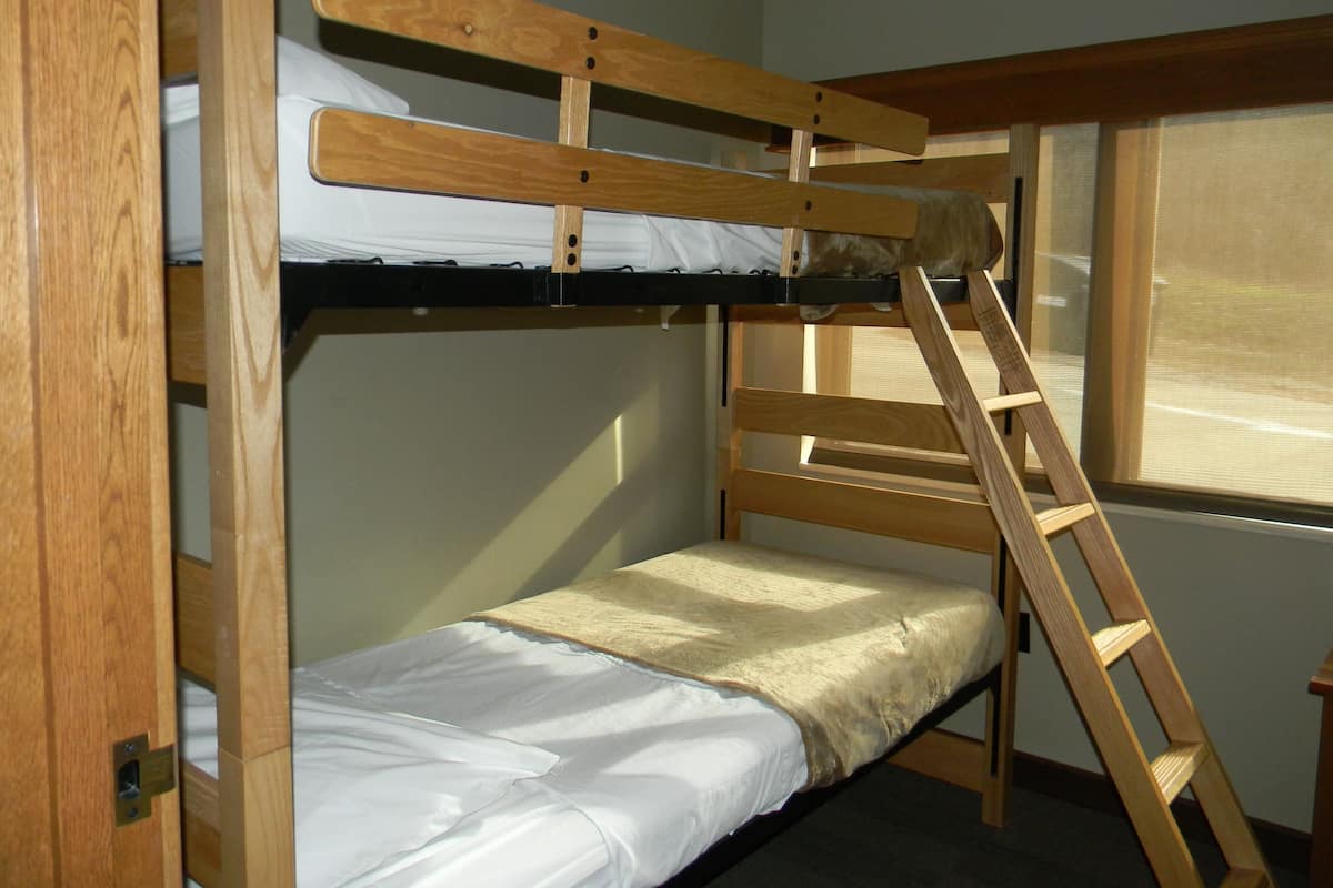 A bunk bed with a wooden ladder, a window with blinds, and a door with a handle.