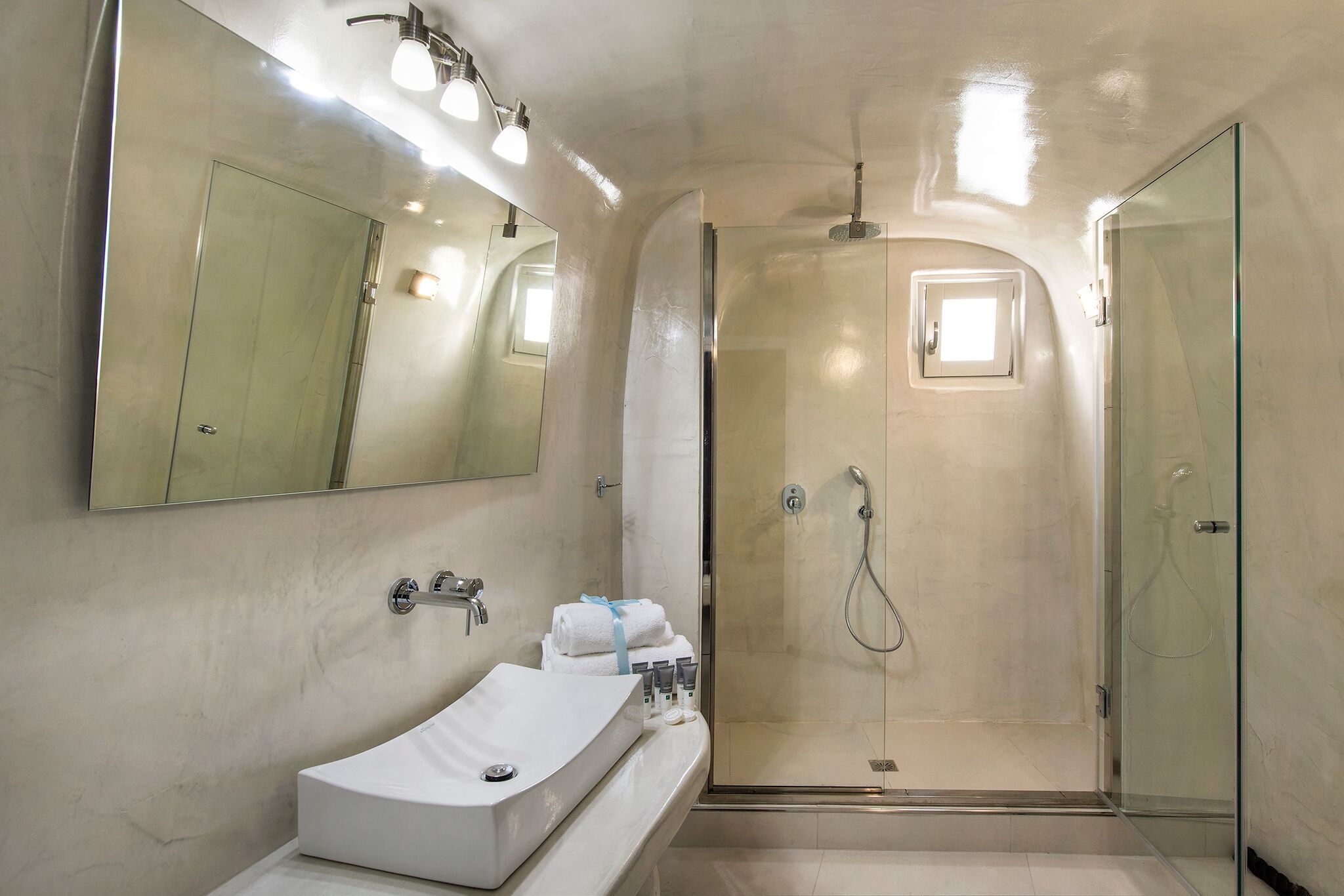 Un baño moderno con un espejo grande, un lavamanos blanco y una ducha con mampara de vidrio.