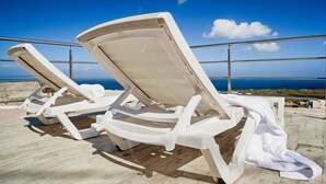 Two white lounge chairs with towels, positioned on a terrace with a view of the sea. - Spilies by Thireas (Santorini)