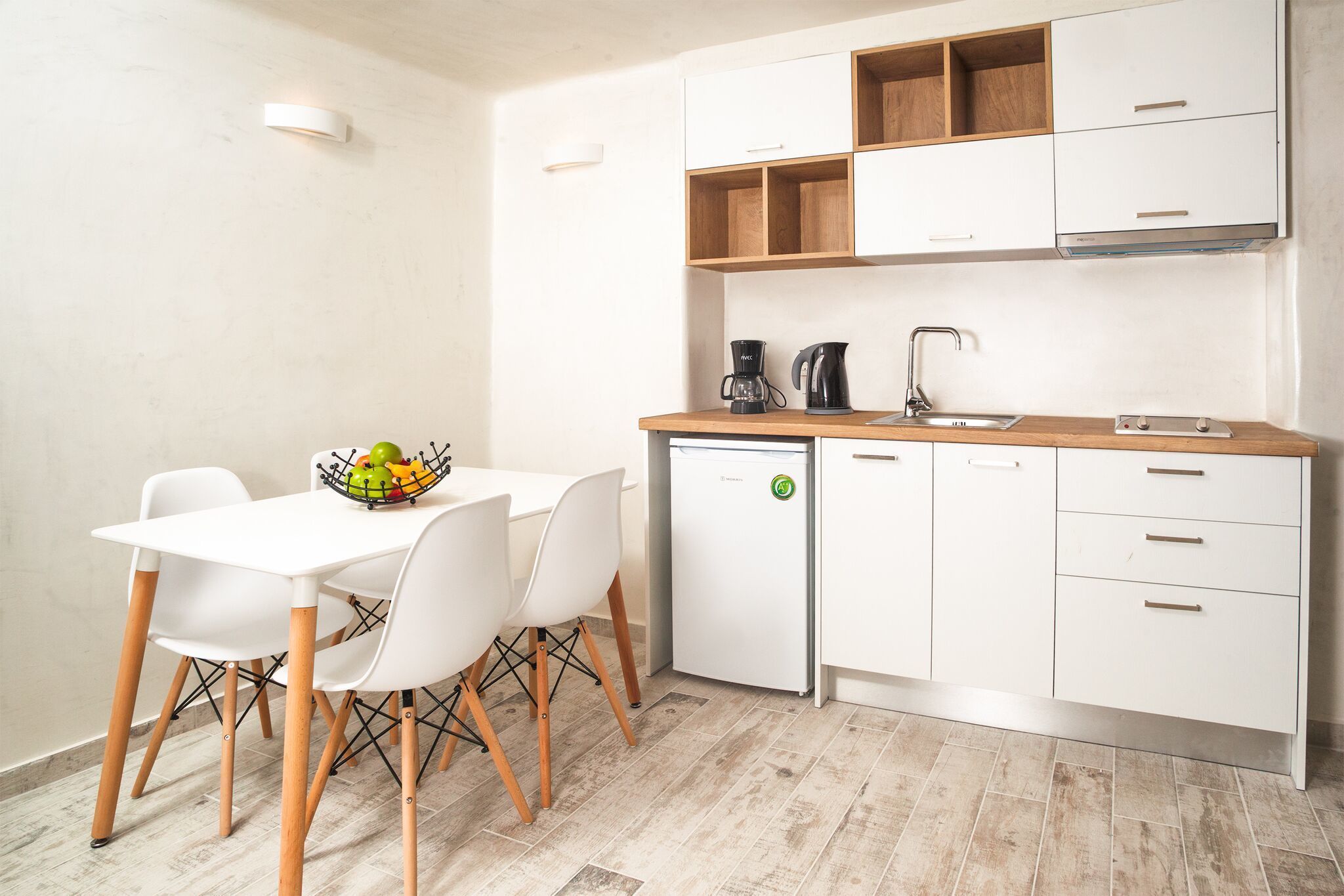 A compact kitchen with white cabinets, a wooden countertop, a sink, and a small refrigerator.