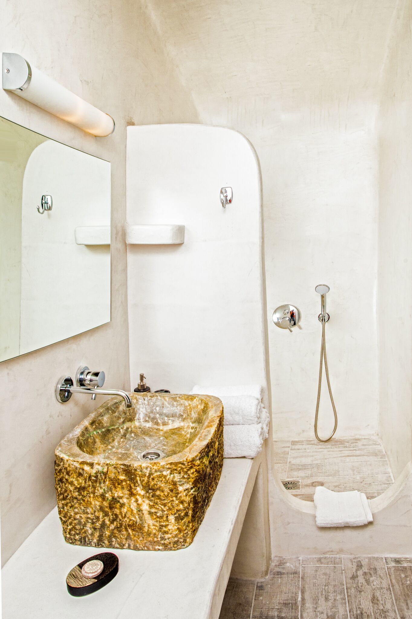 A bathroom with a granite sink, a mirror, a shower, and a towel rack.