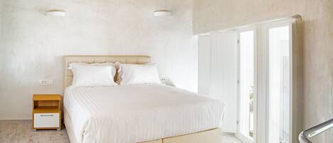 A bedroom with a large bed, a nightstand, and a window with a view.
