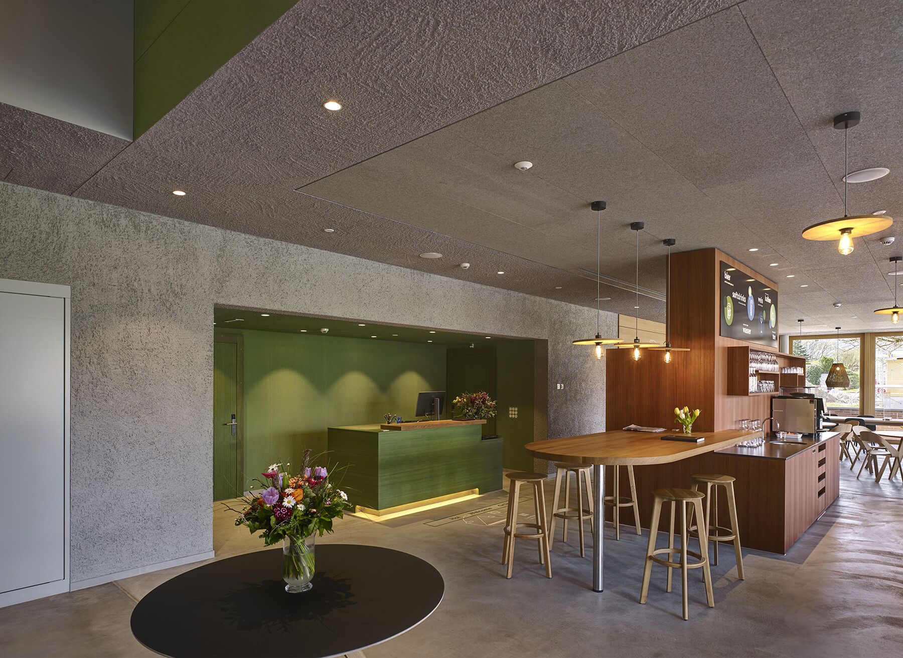 A modern reception area with a green wall, a reception desk, and a bar area with stools.