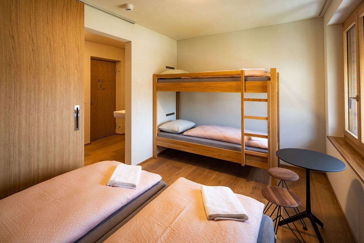 Een kamer met twee eenpersoonsbedden, een stapelbed, een klein tafeltje en een kledingkast.