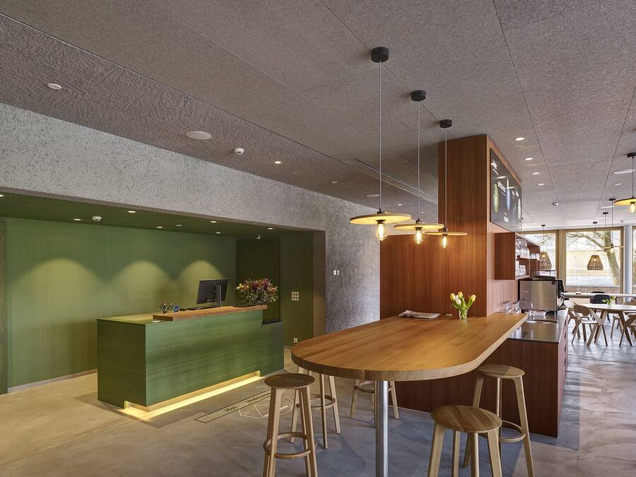Un espace d’accueil moderne avec un comptoir de réception en bois, des tabourets de bar et une grande table à manger.