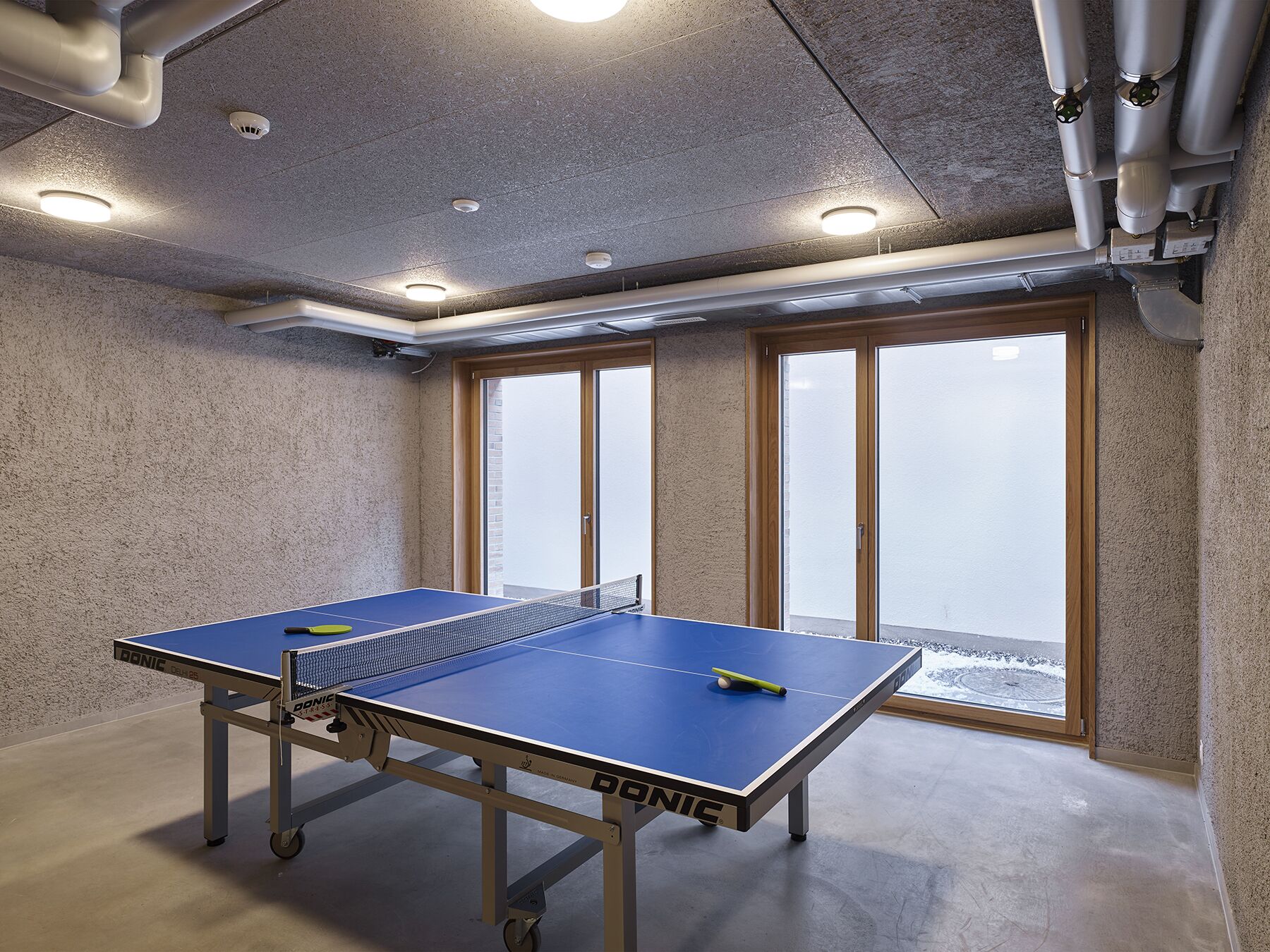 A ping pong table in a room with a concrete ceiling, large windows, and a view of a snowy landscape.