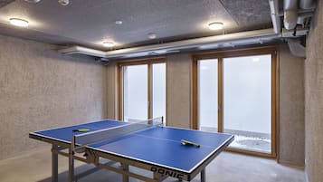 Une table de ping-pong dans une pièce dotée d’un plafond en béton, de grandes fenêtres et offrant une vue sur un paysage enneigé.