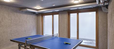 A ping pong table in a room with a concrete ceiling, large windows, and a view of a snowy landscape.