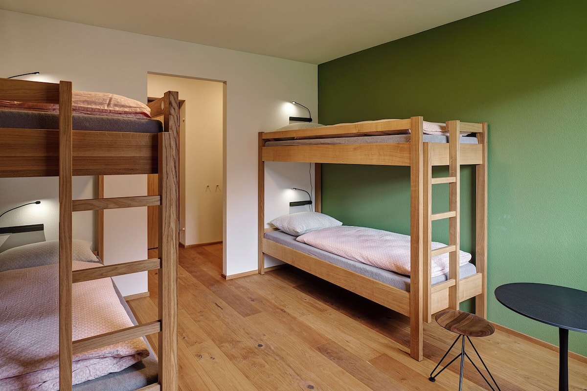Een slaapkamer met een stapelbed, een groene muur, een kleine tafel en een deur naar een andere kamer.