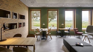 Een modern interieur met een bakstenen muur, houten tafels en stoelen, en grote ramen met uitzicht op groen.