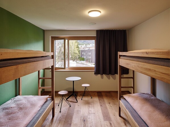 Un dormitorio con literas, una mesita redonda pequeña y una ventana con cortinas.