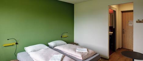 Una habitación con dos camas, una mesita pequeña y una pared verde.