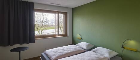 Un dormitorio con cama, una mesita redonda pequeña, una silla, una ventana con cortinas y una pared verde.